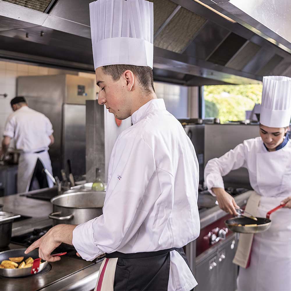 Jeune cuisinier en train de faire cuire des pommes de terre dans une poele